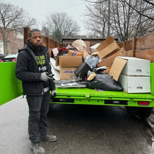 Man in work clothes standing by a trailer filled with junk removal items. Rubble Rumblers